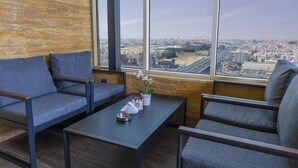 A modern lounge with a large window offering a city view, a small table with a plant, and two grey sofas. - Iridium 70 Hotel (Jeddah)