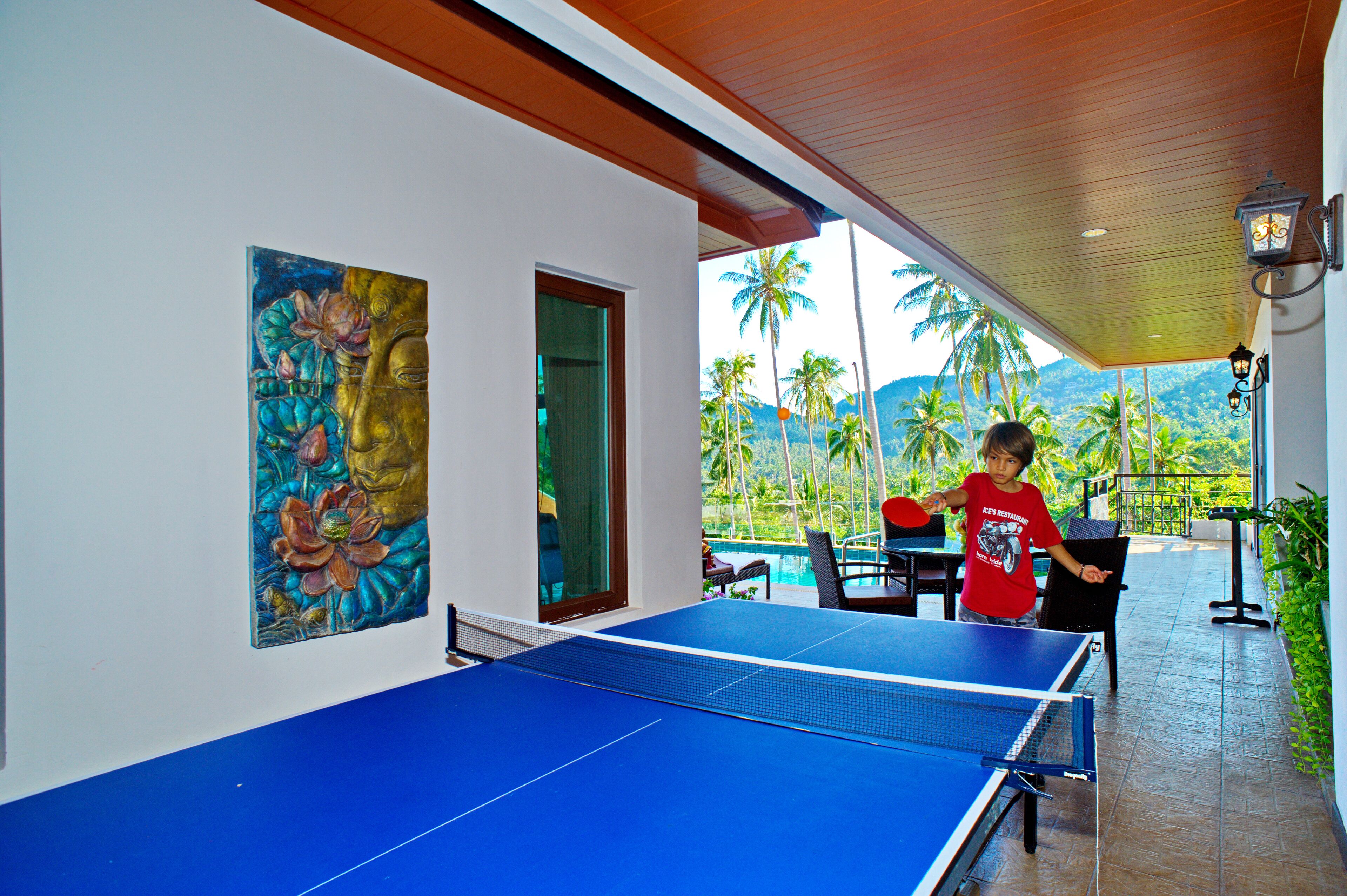 A ping pong table in a covered area with a view of palm trees and mountains.