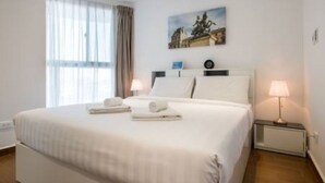Ein Hotelzimmer mit einem großen Bett, zwei Nachttischlampen, einem Bild an der Wand und einem Fenster mit Vorhängen.
