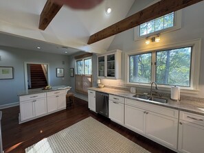 A kitchen with white cabinets, a granite countertop, a dishwasher, a sink, and a window with a view of trees.