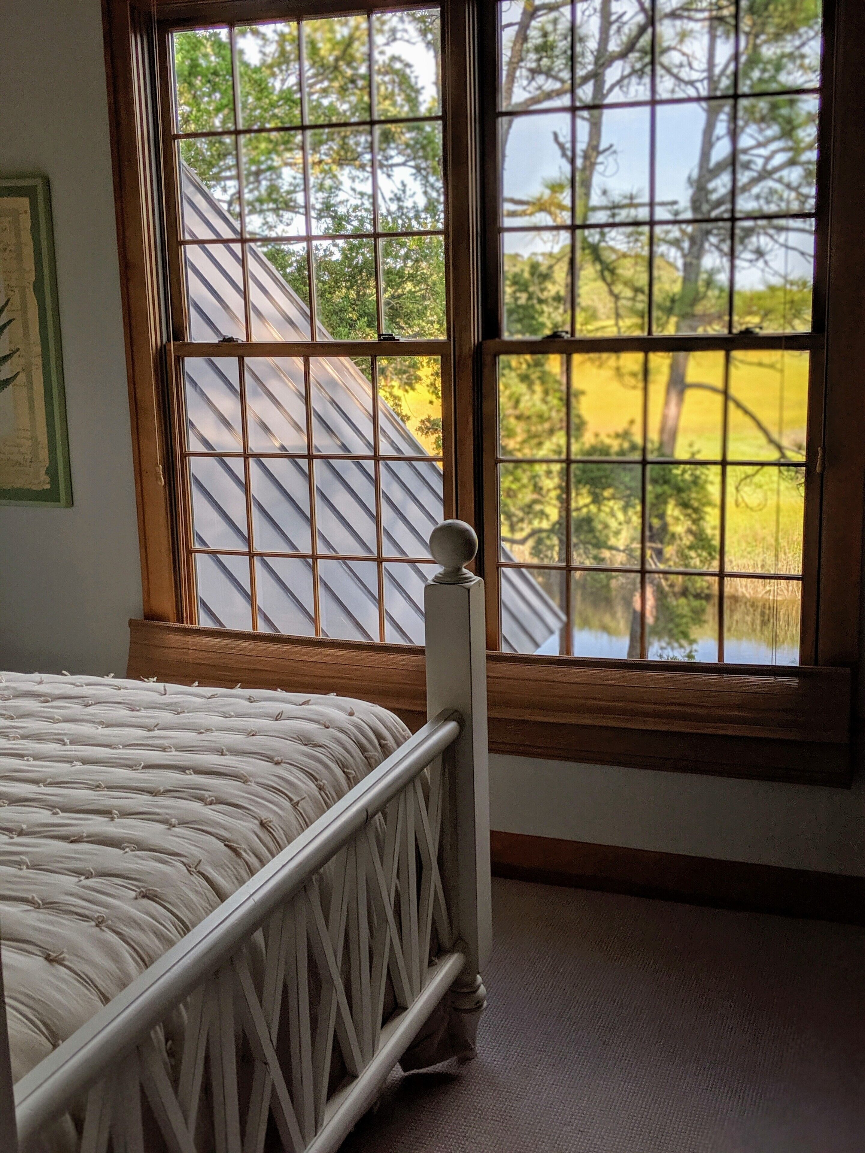 A bedroom with a bed, a window with a view of trees, and a wooden headboard.