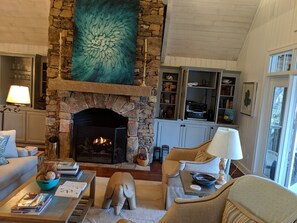 Cozy living room with a fireplace, comfortable seating area, and a bookshelf filled with books and decorative items.