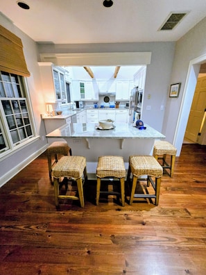 A kitchen with a central island, wooden stools, and a view into adjacent rooms.