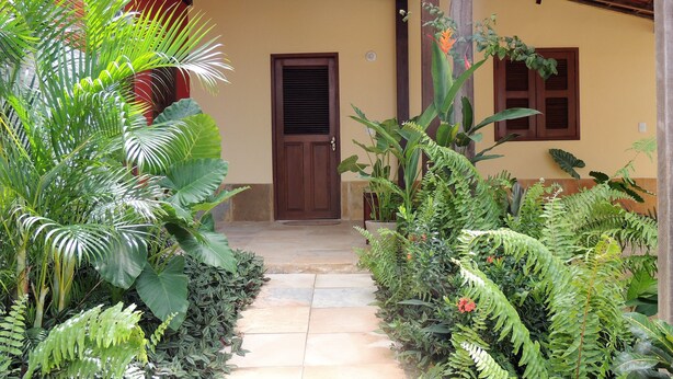 A pathway leading to a building with a wooden door and windows, surrounded by lush greenery and plants. - Our House in Jeri 1 (Jijoca de Jericoacoara)