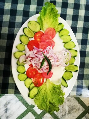 A plate of sliced vegetables including cucumbers, tomatoes, and onions, arranged on a white plate.