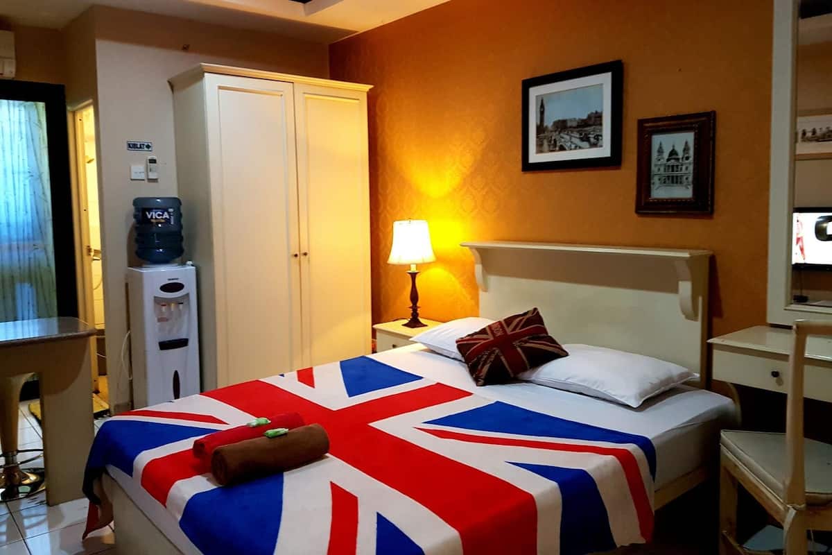 Ein Hotelzimmer mit einem Bett, das mit einer Bettdecke mit Union Jack Muster versehen ist, einer Nachttischlampe, einem Wasserspender und einem gerahmten Bild an der Wand.