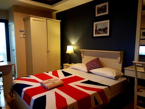 Ett hotellrum med en säng som har ett sängöverkast med Union Jack-mönster, en vit sänggavel och två kuddar. Det finns ett nattduksbord med en lampa, en garderob och ett skrivbord med en stol.