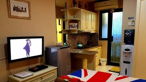 Ein kleines Hotelzimmer mit einem Bett, das mit einer Decke mit Union Jack Muster versehen ist, einer kleinen Küchenzeile inklusive Kühlschrank, Wasserkocher und Wasserspender.