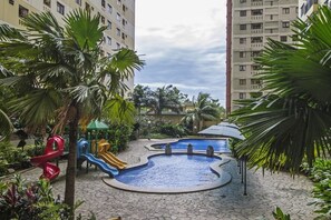 En lekplats för barn med rutschkanor och en liten pool, omgiven av palmer och en asfalterad gångväg.