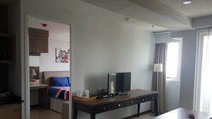 Ein Hotelzimmer mit Bett, Schreibtisch mit Fernseher, Fenster mit Vorhängen und einer Tür zu einem anderen Raum.