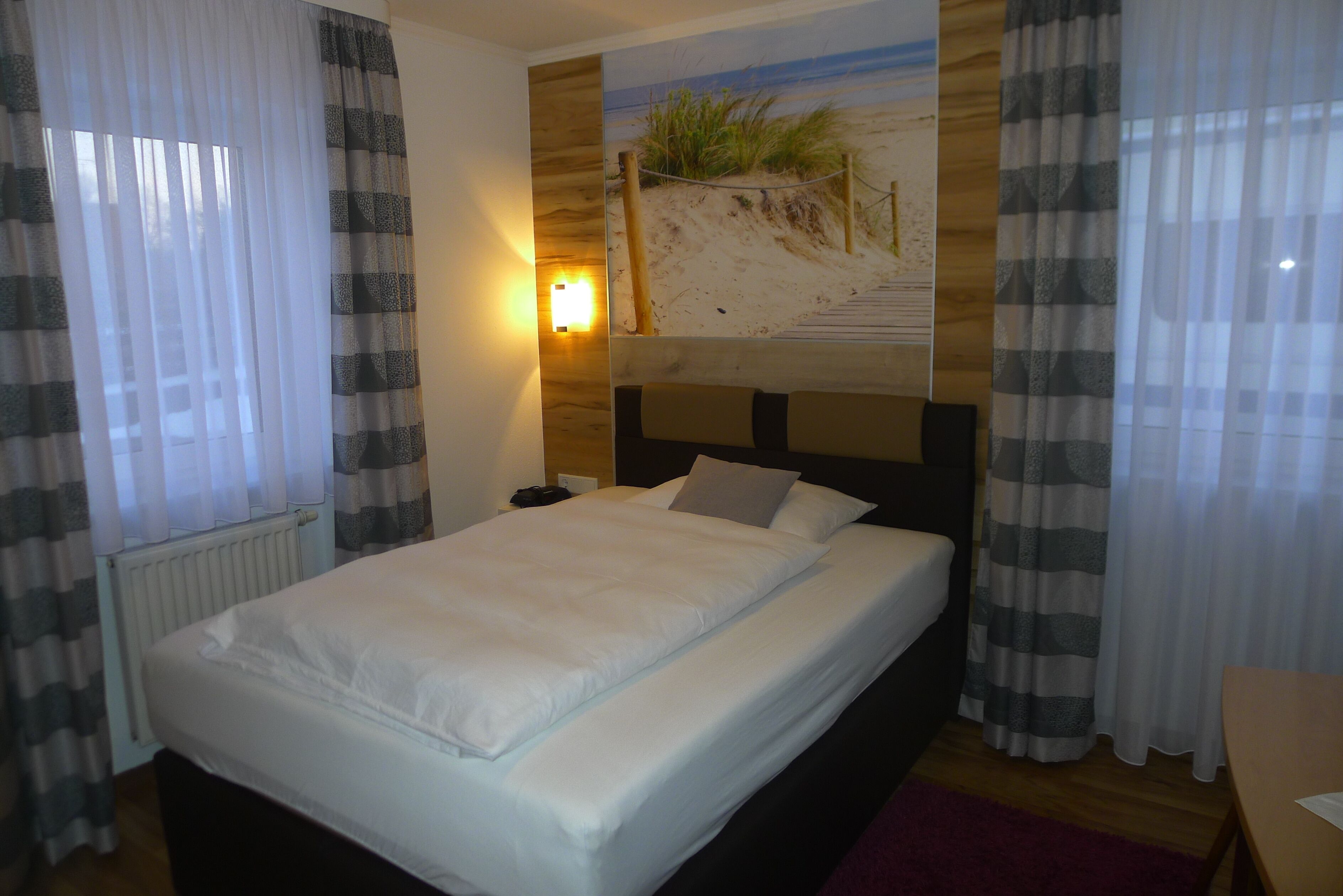 A neatly made bed with white linens, a headboard, and a nightstand with a lamp.