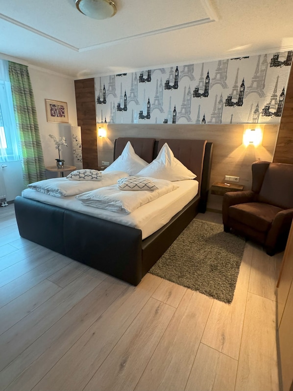 Un dormitorio moderno con una cama grande, un cabecero marrón, suelo de madera, alfombra verde y una pared con papel tapiz de un paisaje urbano.