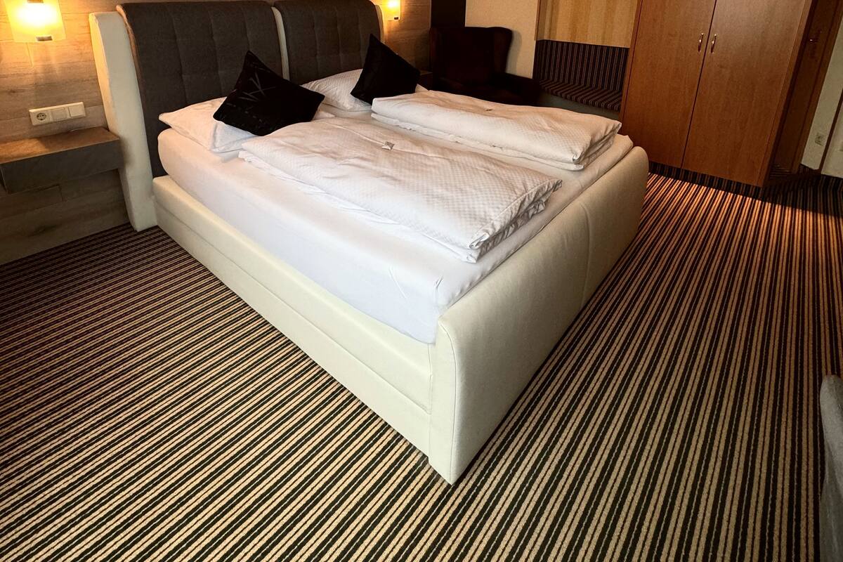 A hotel room with a large bed, a wooden headboard, a bedside table, a hanging light, and a wardrobe.
