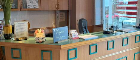 A hotel reception desk with a wooden counter, a glass display case, and a window with red blinds.