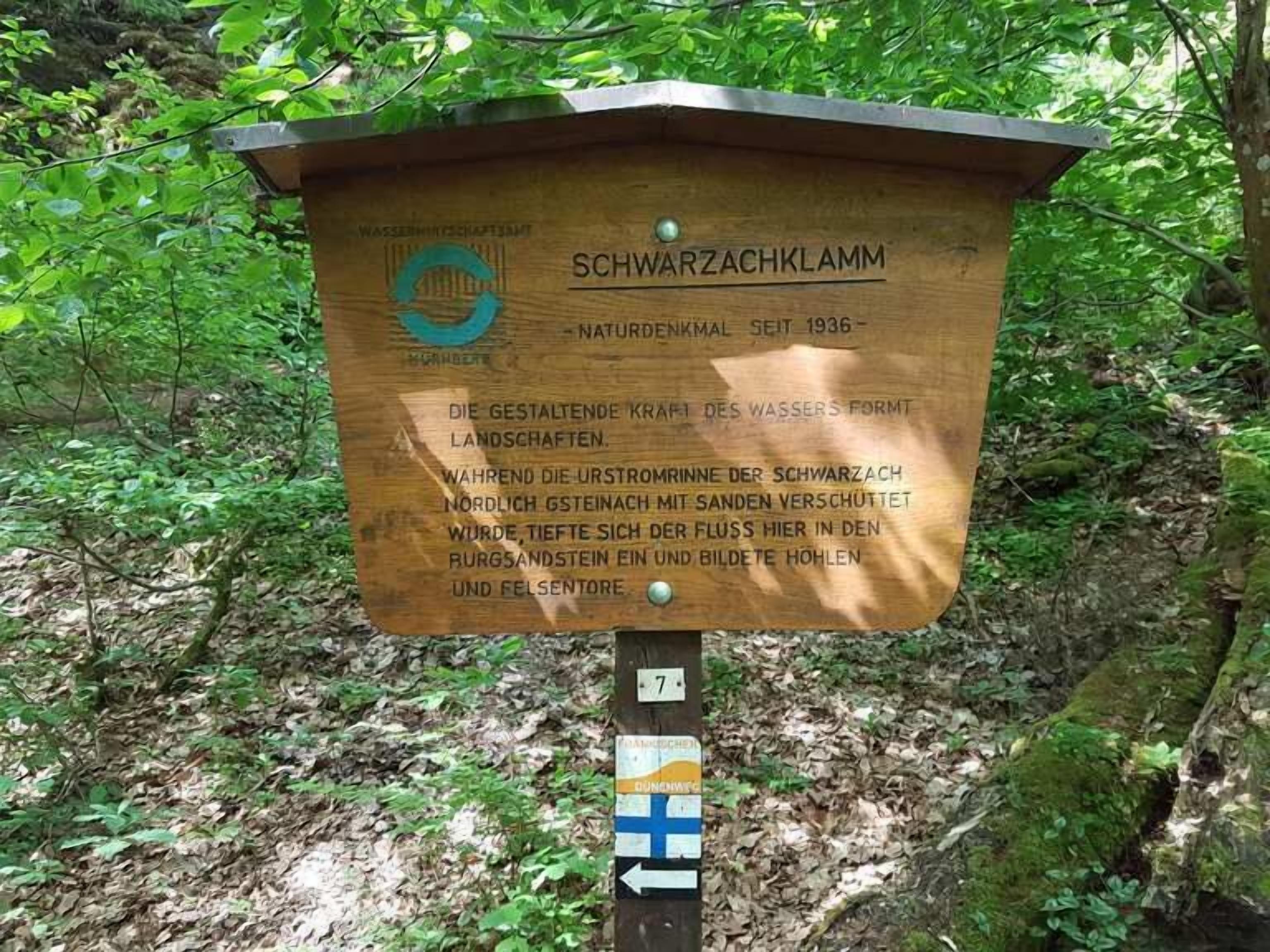 A wooden sign with text in a foreign language, surrounded by greenery.