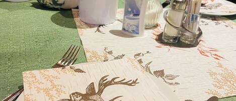 A table set with a plate, spoon, knife, and fork, a bottle of Süssli, a salt shaker, and a lemon wedge on a tablecloth with a floral pattern.