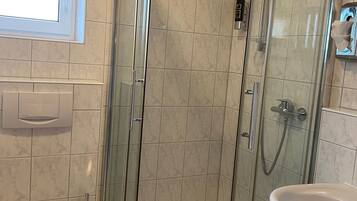 A bathroom with a glass-enclosed shower, a toilet, and a sink.