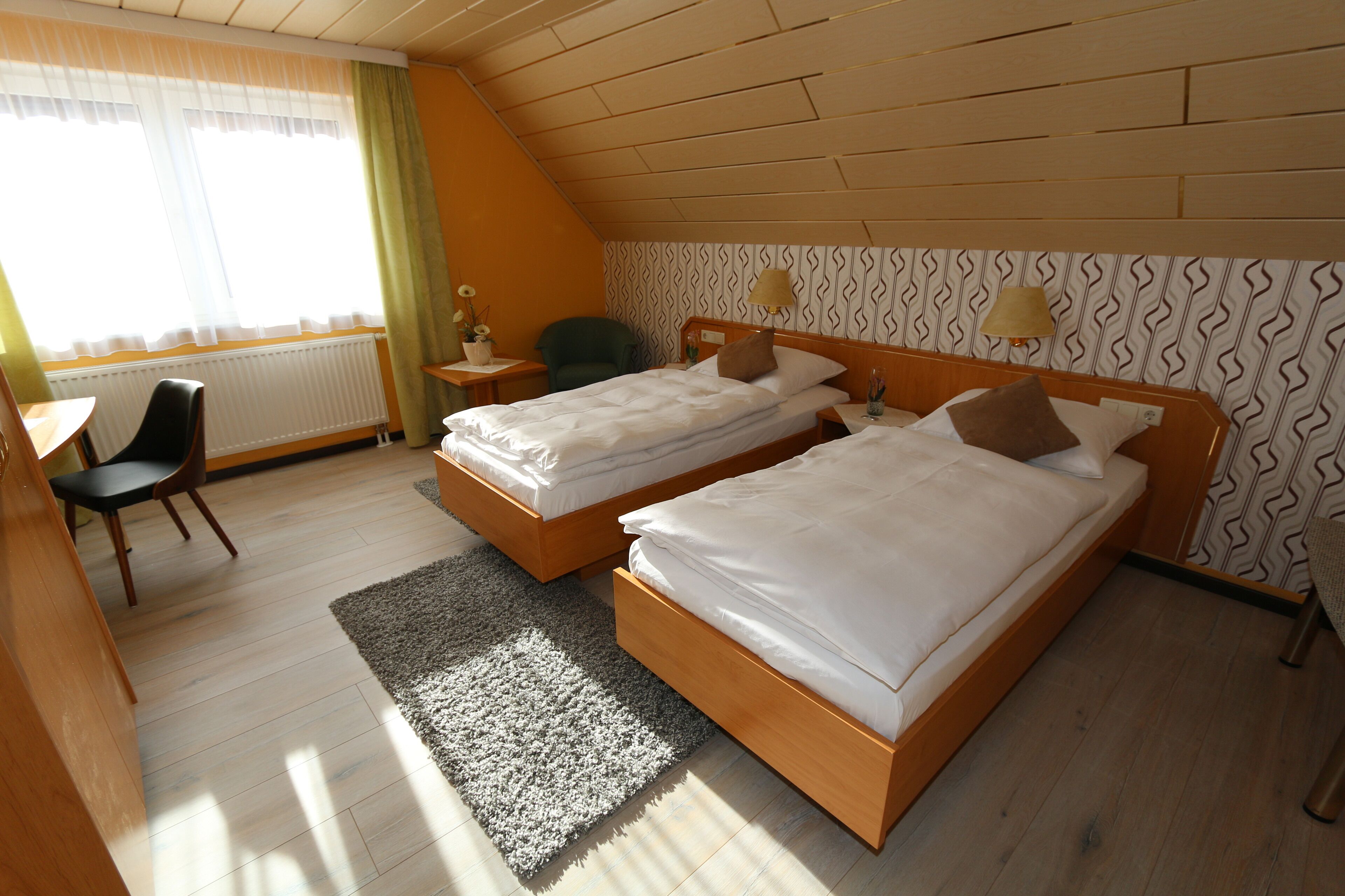 A hotel room with two beds, a desk, a chair, and a window with curtains.