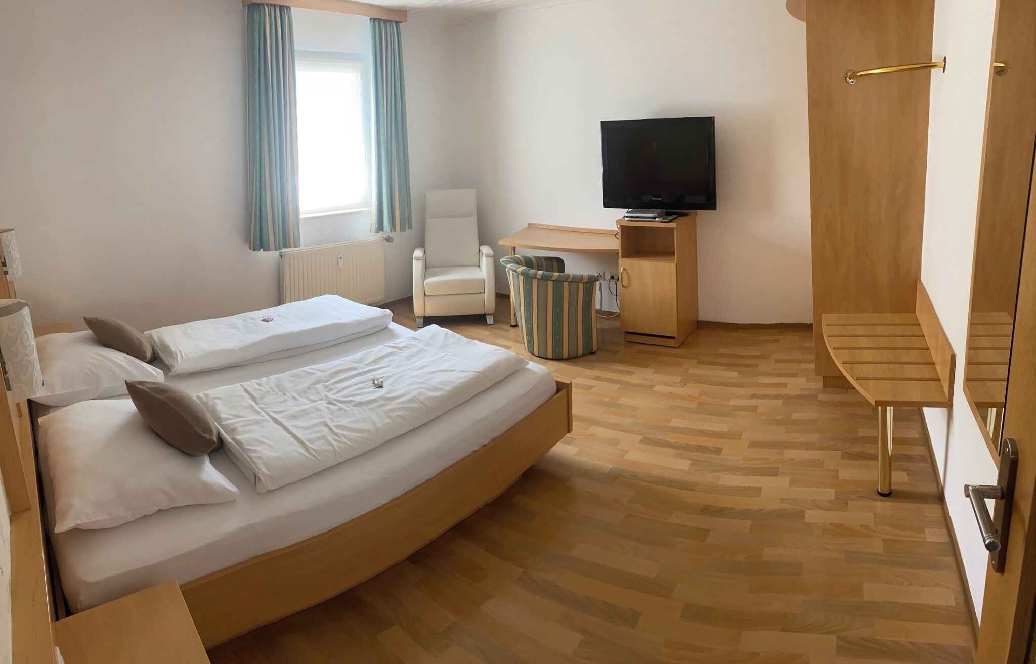 A hotel room with a bed, a chair, a desk, a television, and a wardrobe.