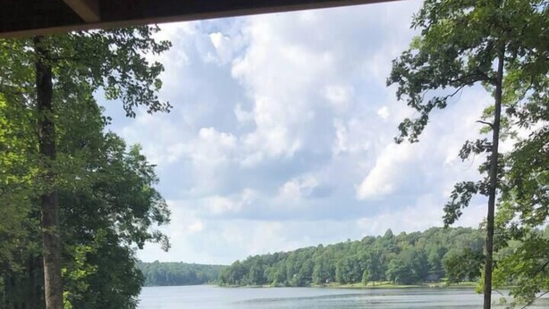 A lakeside view from a cabin with a dock extending into the water, surrounded by trees and a grassy area. - 2 Bedroom Lakefront Cabin with Hot Tub! (Brookport)