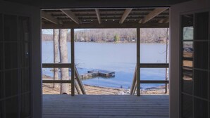 A view through a window of a building with a wooden deck, a dock extending into a lake, and trees in the background. - 2 Bedroom Lakefront Cabin with Hot Tub! (Brookport)