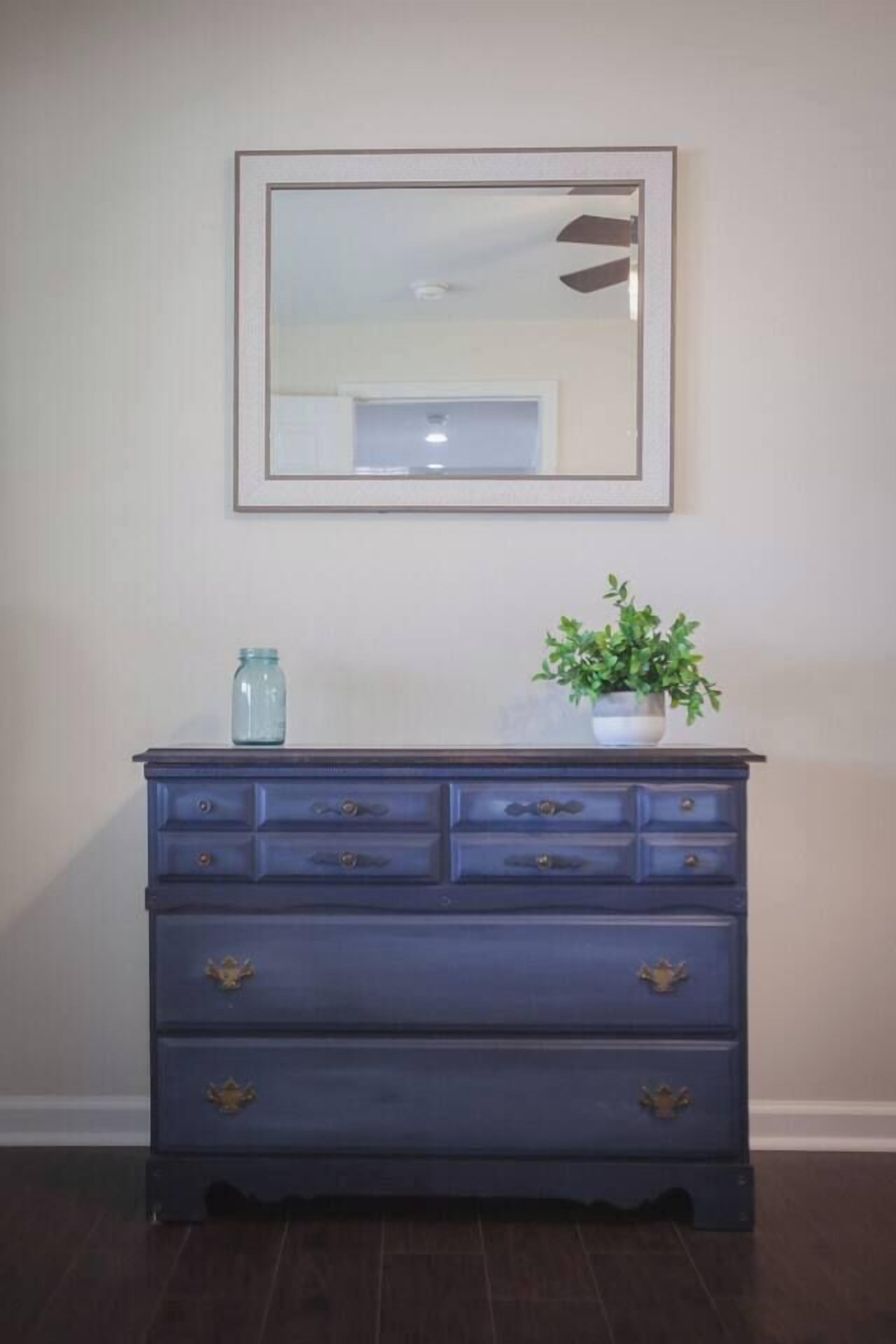 Een donkerblauwe dressoir met gouden handgrepen, een kleine potplant en een blauwe pot erop.