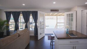 A spacious living area with a sofa, a dining table, and a kitchen area with a countertop and cabinets. - 2 Bedroom Lakefront Cabin with Hot Tub! (Brookport)