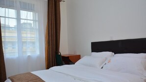 A hotel room with a bed, a nightstand, a window with curtains, and a view of buildings outside. - Sunway Hotel Nairobi - YOHOH (Nairobi)