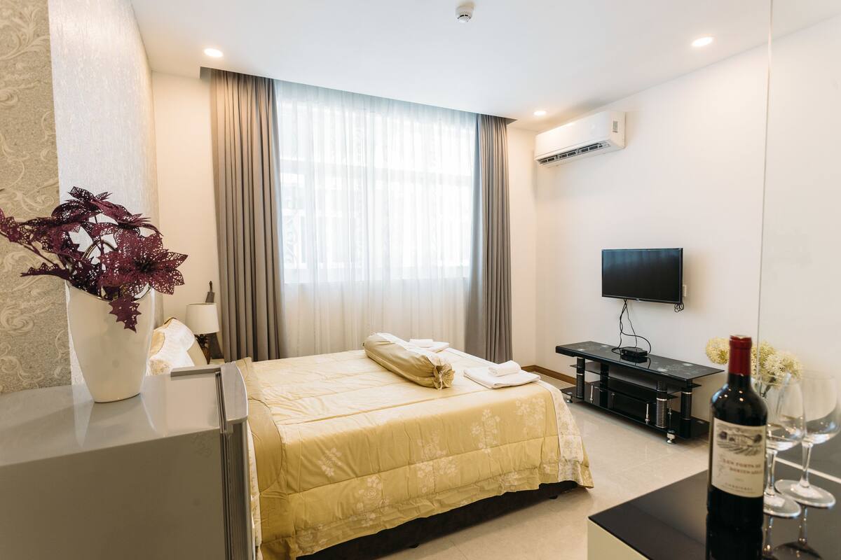 A hotel room with a bed, a TV, a wine bottle, and a vase with flowers.