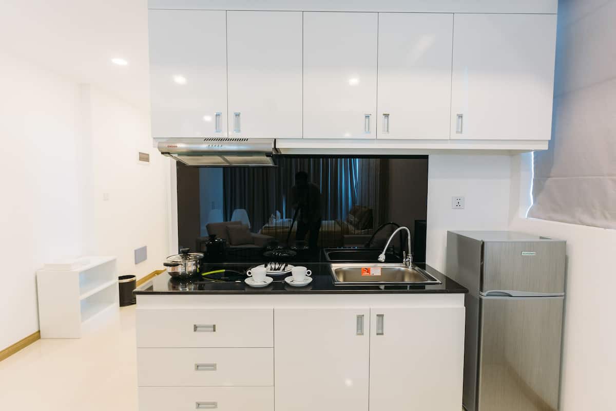 A modern kitchen with white cabinets, a stainless steel refrigerator, and a black countertop.