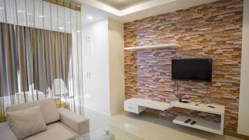A modern living room with a sofa, a glass coffee table, a TV mounted on a stone-patterned wall, and a white entertainment unit with remote controls.