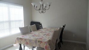 Une salle à manger avec une table recouverte d’une nappe à motifs floraux, entourée de chaises, et un lustre au-dessus.