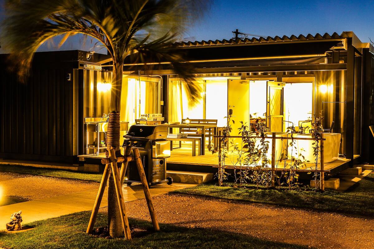 A well-lit outdoor patio area with a grill, seating, and a small garden.