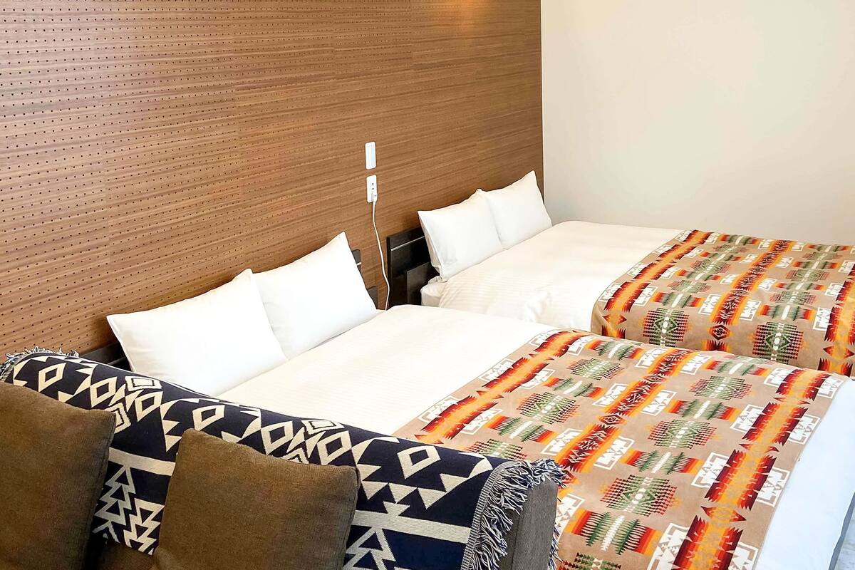 A hotel room with two beds, each with white linens and patterned blankets.