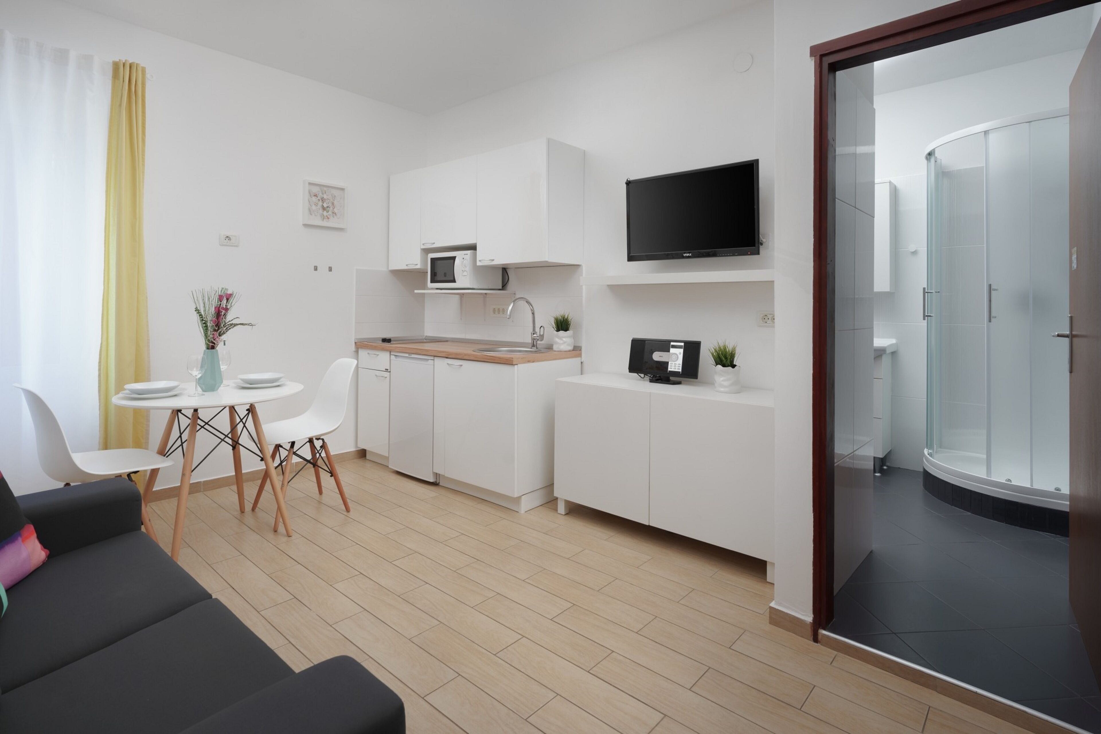 A modern, compact living space with a kitchenette, a dining area, and a glass-enclosed shower.