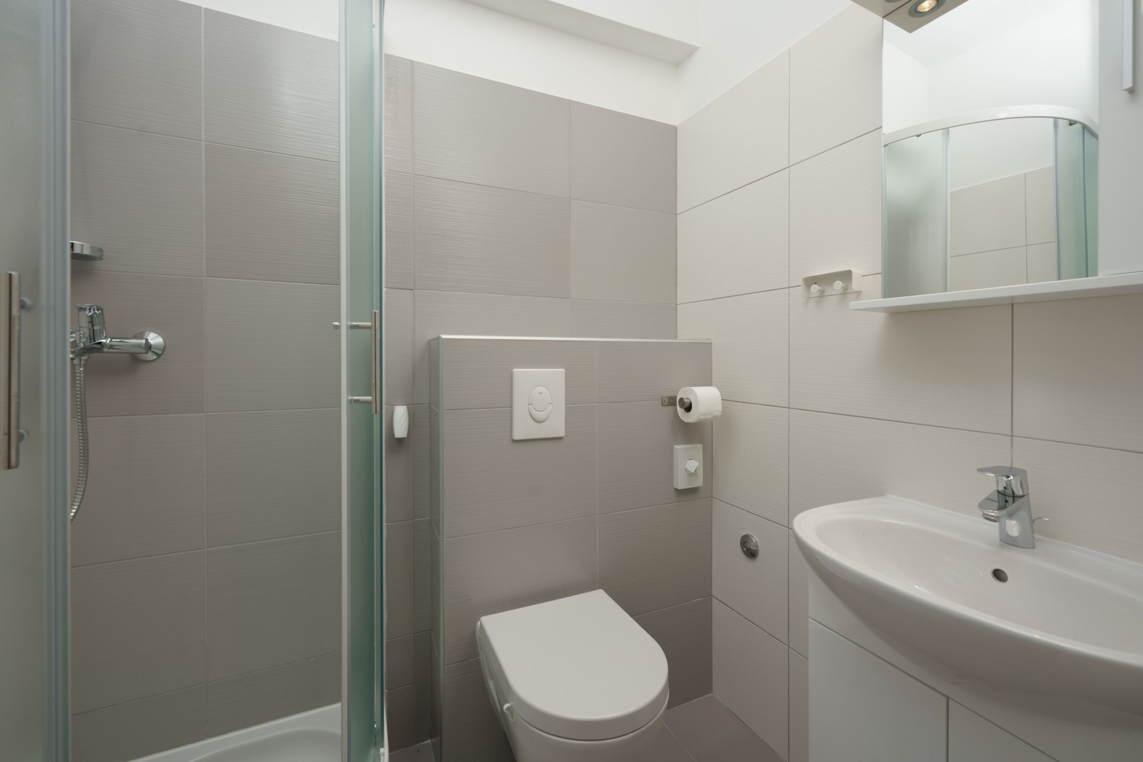 A modern bathroom with a glass shower enclosure, a toilet, and a sink with a mirror above it.