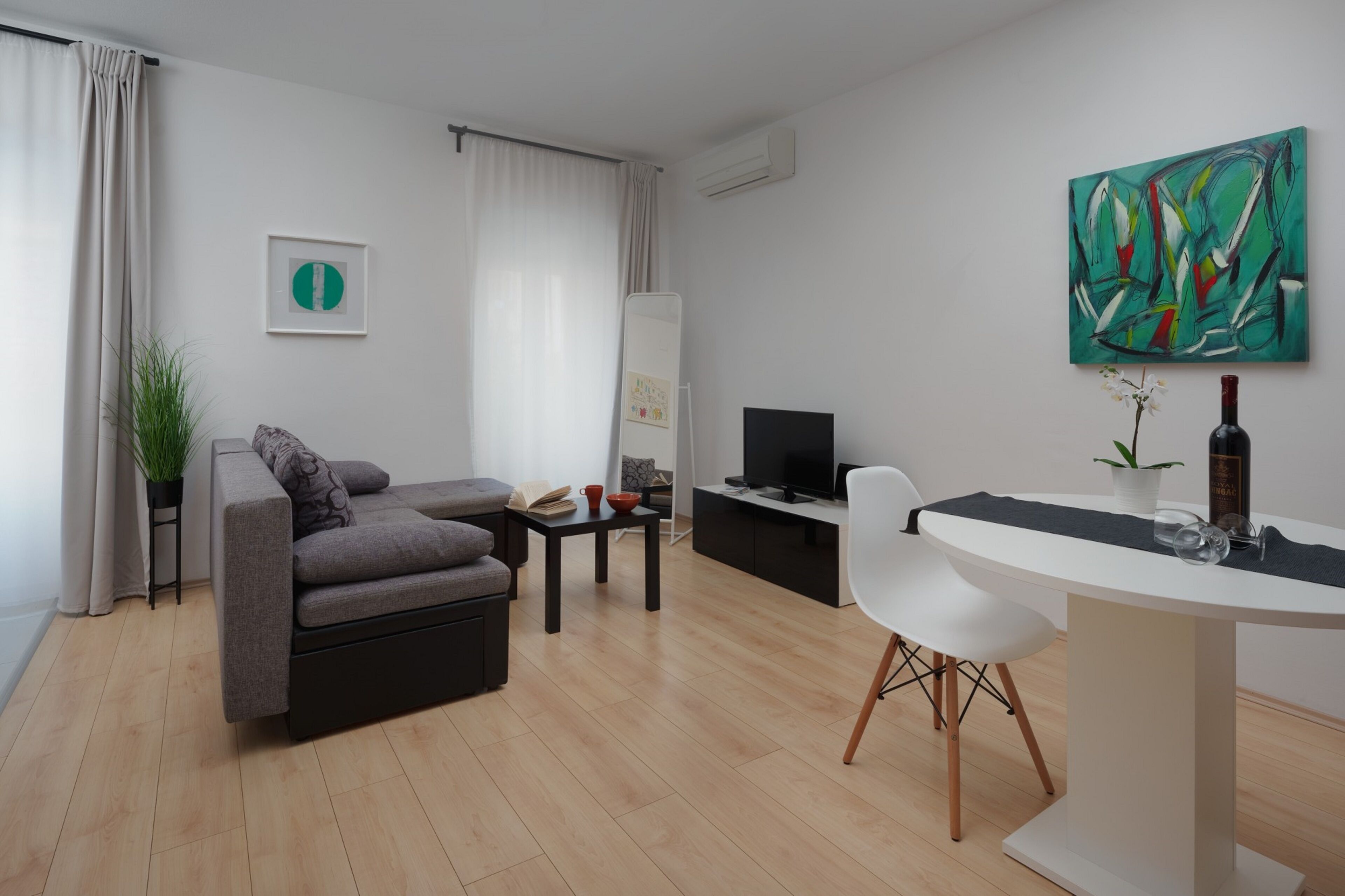 Una sala de estar moderna con un sofá gris, una mesita, una silla blanca, un televisor y un cuadro en la pared.