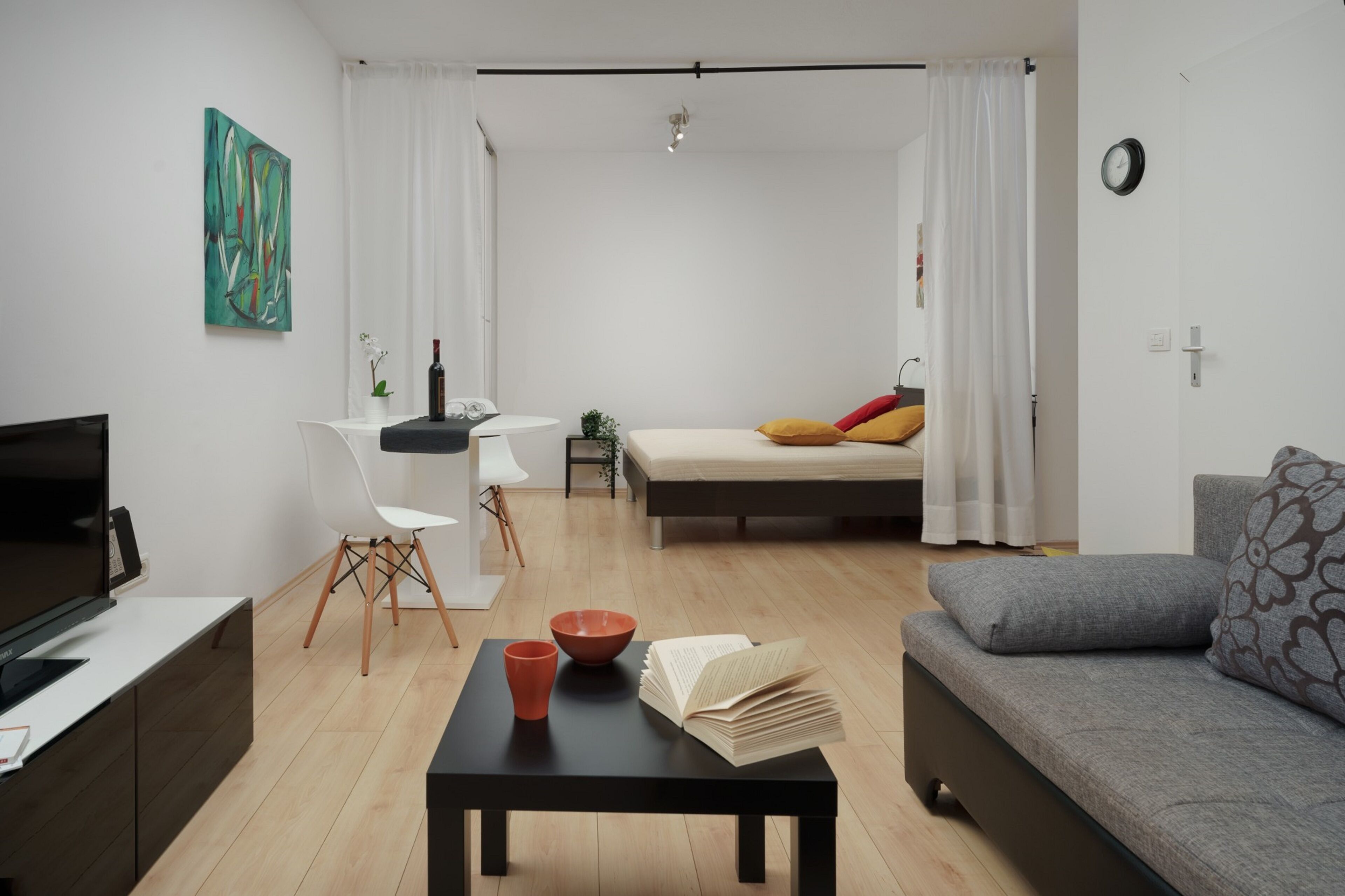 Una sala de estar moderna con un sofá, una mesa de centro con libros y un cuenco, un televisor y un comedor con una silla y una mesa.