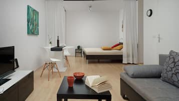 Una sala de estar moderna con un sofá, una mesa de centro con libros y un cuenco, un televisor y un comedor con una silla y una mesa.