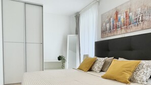 Une chambre à coucher avec un lit, une tête de lit noire et un tableau représentant un paysage urbain accroché au mur.