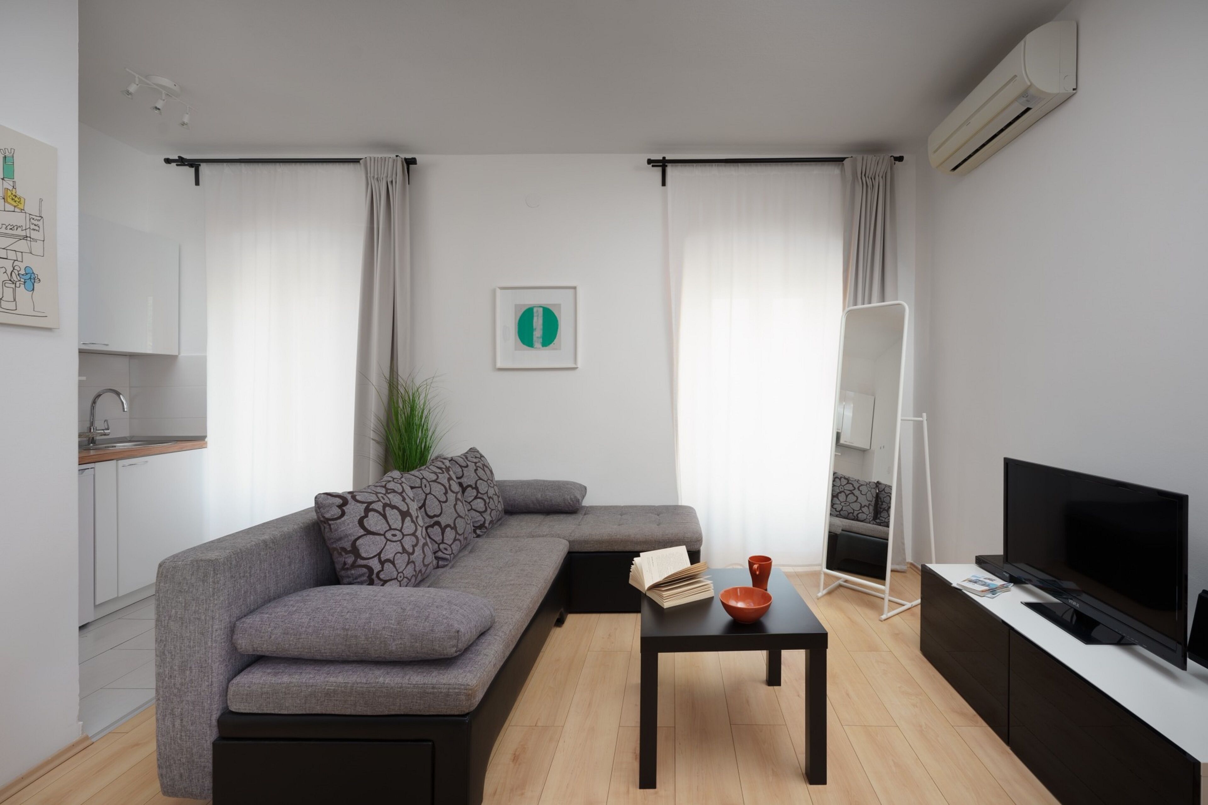 A modern living room with a grey sofa, a black coffee table, a flat-screen TV, and a small side table.
