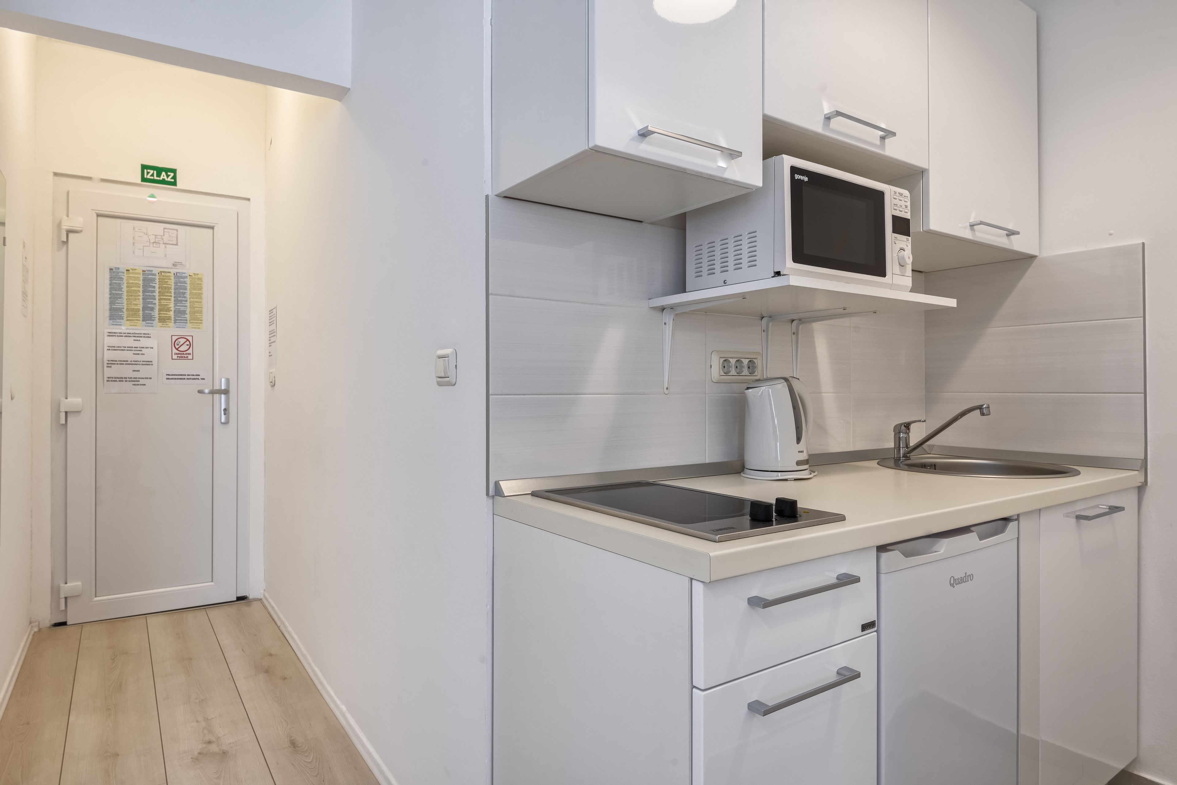 Une cuisine moderne avec des meubles blancs, un four à micro-ondes, une bouilloire et un évier.