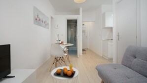 Una sala de estar moderna con un sofá gris, un televisor de pantalla plana, una zona de comedor con mesa y sillas, y una cocina al fondo.