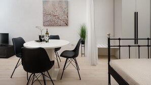 Un dormitorio moderno con cama, mesita de noche, televisor y rincón comedor con sillas y mesa.
