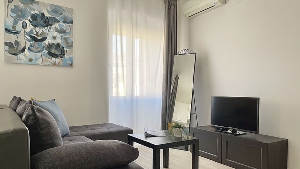 Una sala moderna con un sofá, una mesa de centro, un televisor y un espejo.