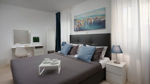 Una habitación de hotel moderna con una cama grande, un escritorio y una silla. Hay un cuadro en la pared y una lámpara en la mesita de noche.