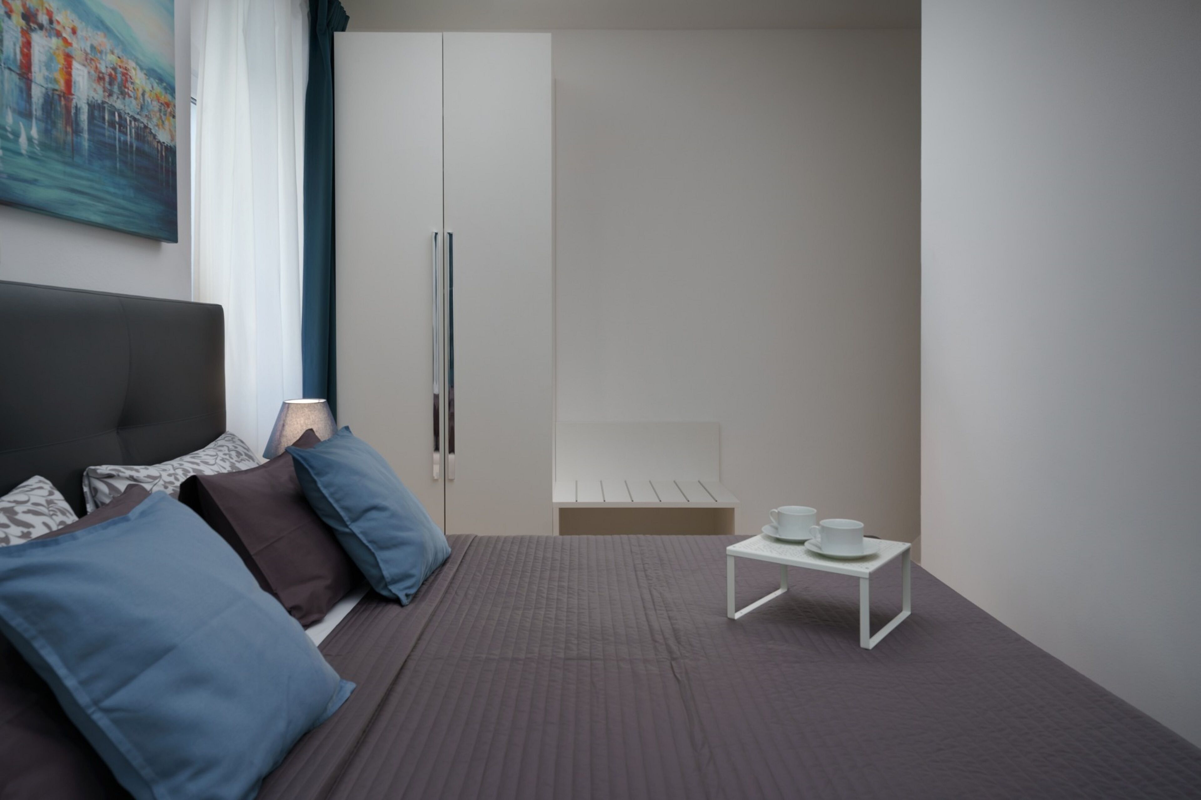 A modern hotel room with a bed, a small table with cups, and a wardrobe.