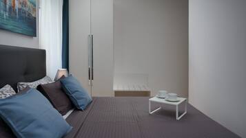 A modern hotel room with a bed, a small table with cups, and a wardrobe.
