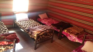 A room with three beds, each with different patterned bedding. There is a window allowing natural light, and the room has a striped red and green wall. - Rum Road - Hostel (Wadi Rum)