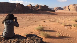 A person taking a photo of a desert landscape with rocky formations and a clear sky. - Rum Road - Hostel (Wadi Rum)